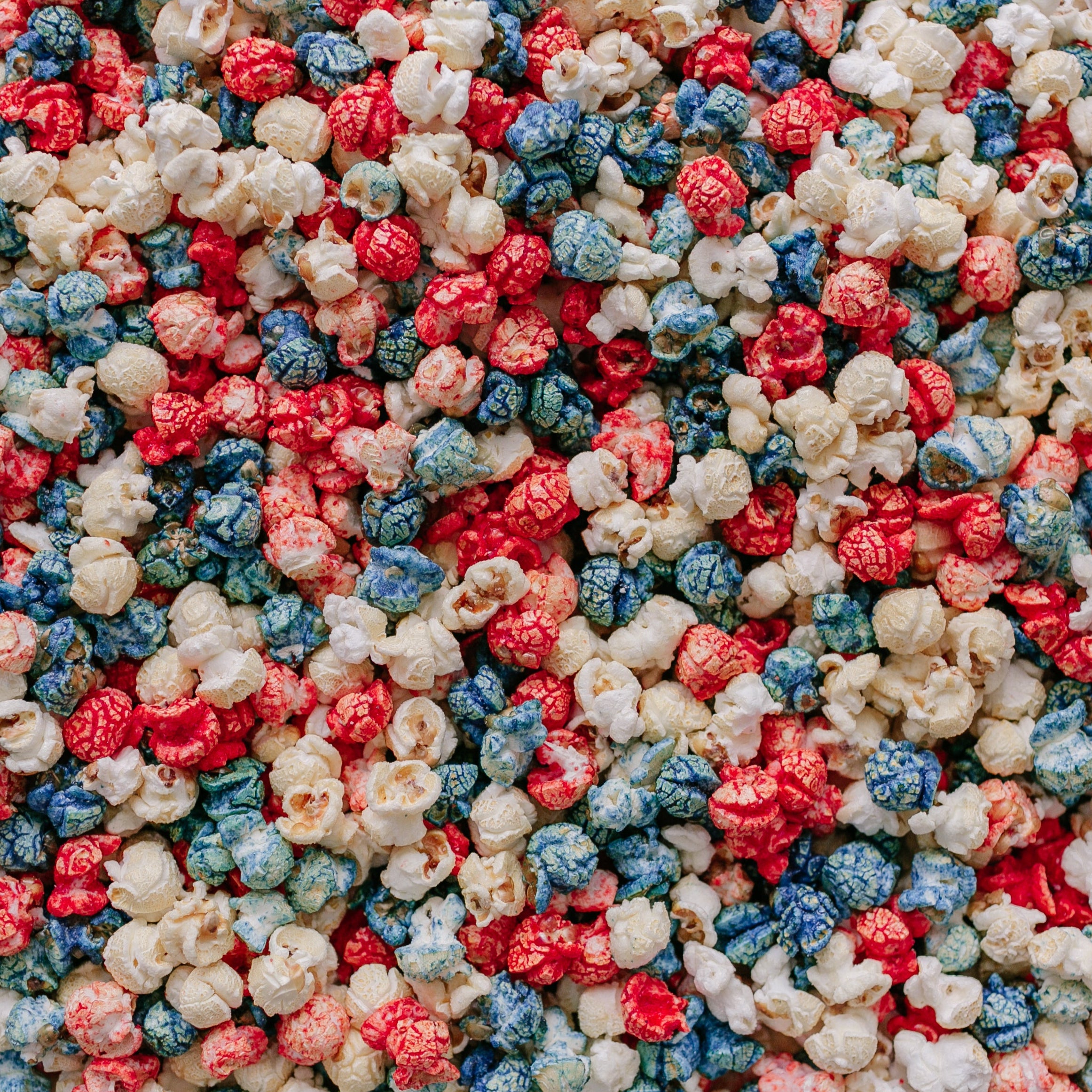 A close-up image of colorful popcorn kernels with red, blue, and white colors, resembling the colors of the American flag, indicating a patriotic theme.